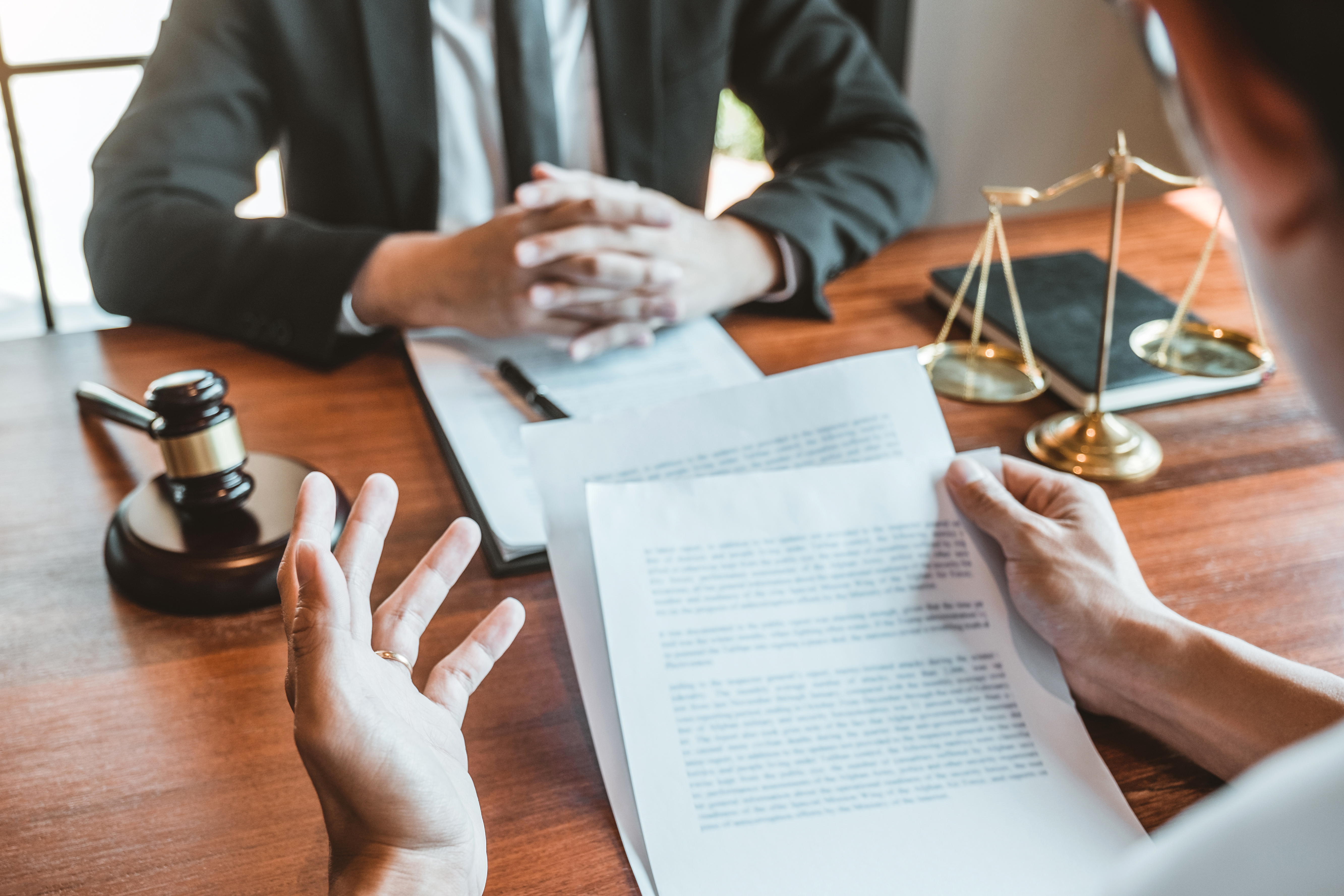 Two people discussing legal documents at a desk with a gavel and scales of justice nearby.