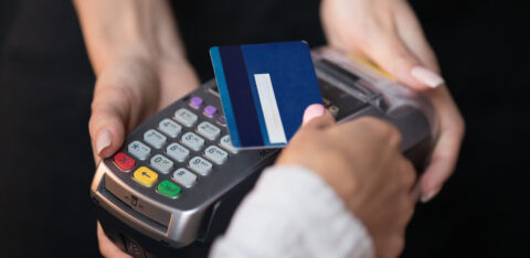 Close-up of a person swiping a blue credit card through a payment terminal held by a cashier.