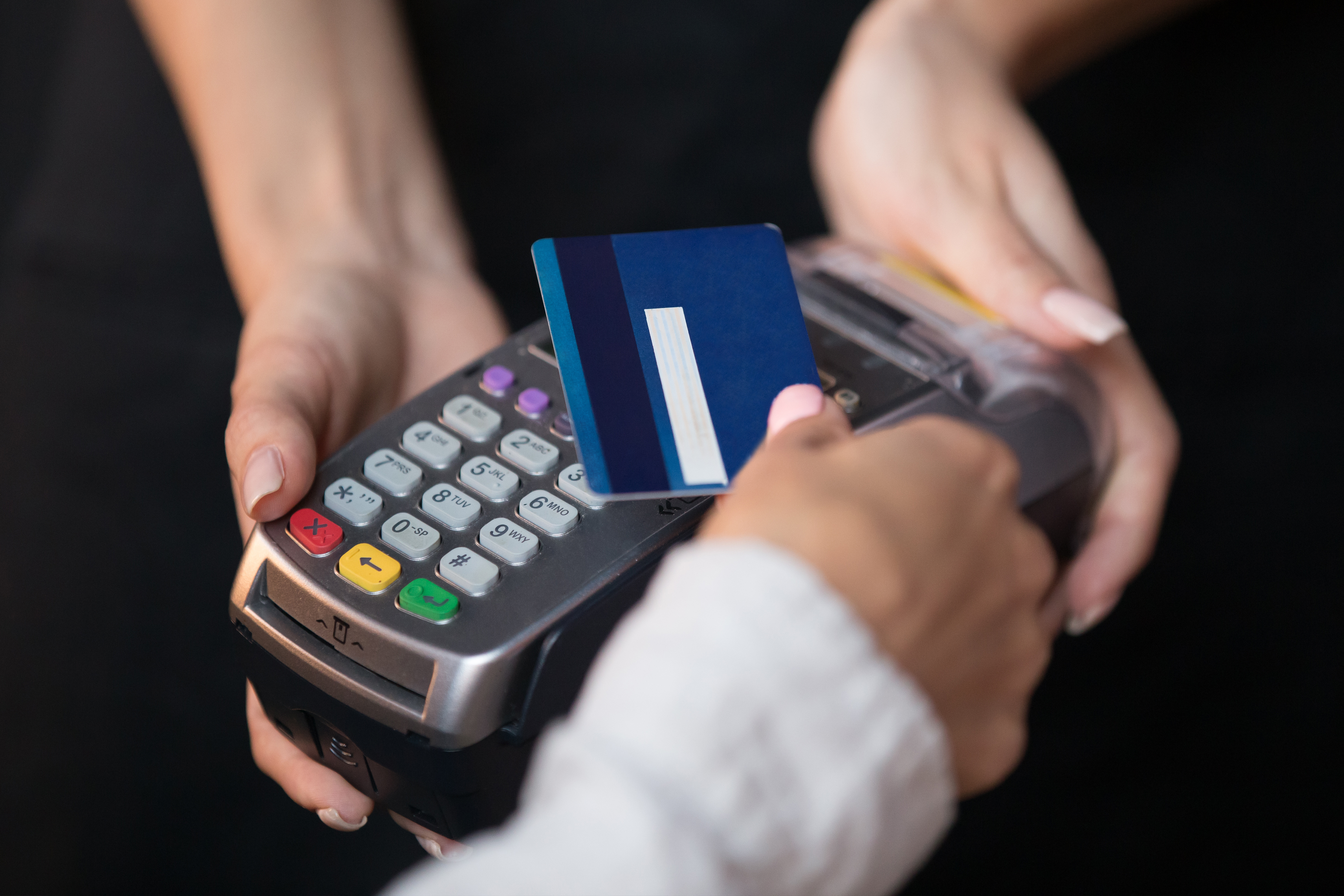 Close-up of a person swiping a blue credit card through a payment terminal held by a cashier.