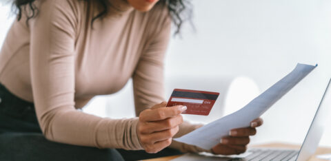 Woman reviewing a bill while holding a credit card, with a calculator and laptop on a desk.
