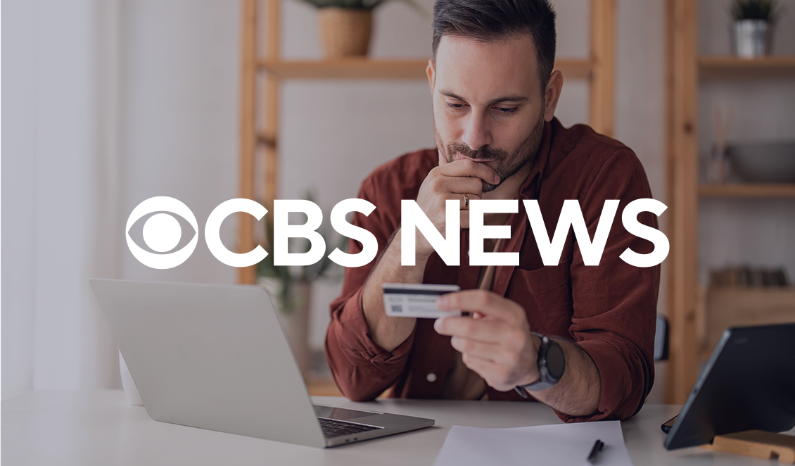 Man reviewing credit card statement while using laptop, with CBS News logo overlayed