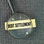 Magnifying glass focusing on the words ‘Debt Settlement’ written on a label