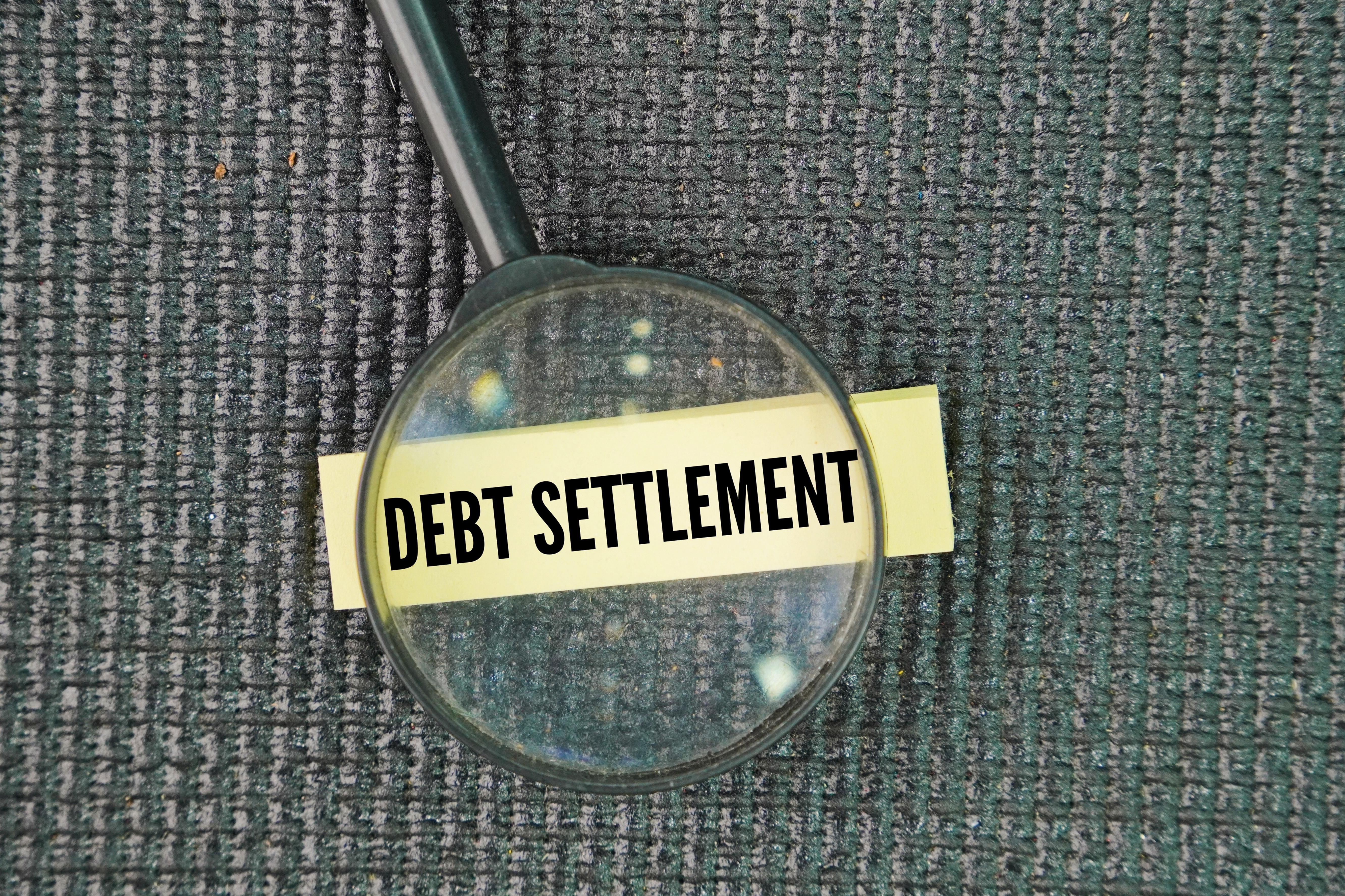 Magnifying glass focusing on the words ‘Debt Settlement’ written on a label