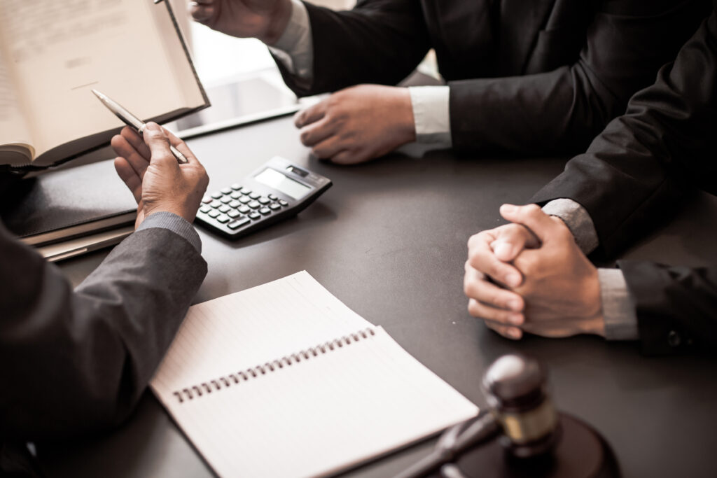 Close-up of people in suits meeting at a desk with legal documents, a calculator, and a gavel.