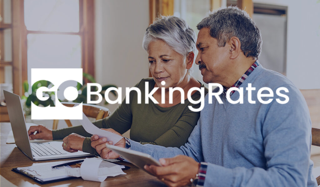 Older couple reviewing bills together at a kitchen table with a laptop, with the GoBankingRates logo overlayed on the image.