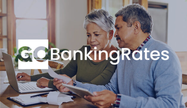Older couple reviewing bills together at a kitchen table with a laptop, with the GoBankingRates logo overlayed on the image.