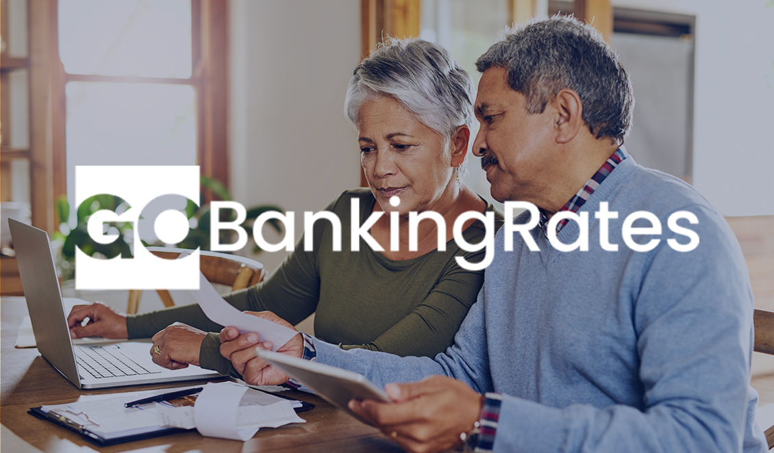 Older couple reviewing bills together at a kitchen table with a laptop, with the GoBankingRates logo overlayed on the image.