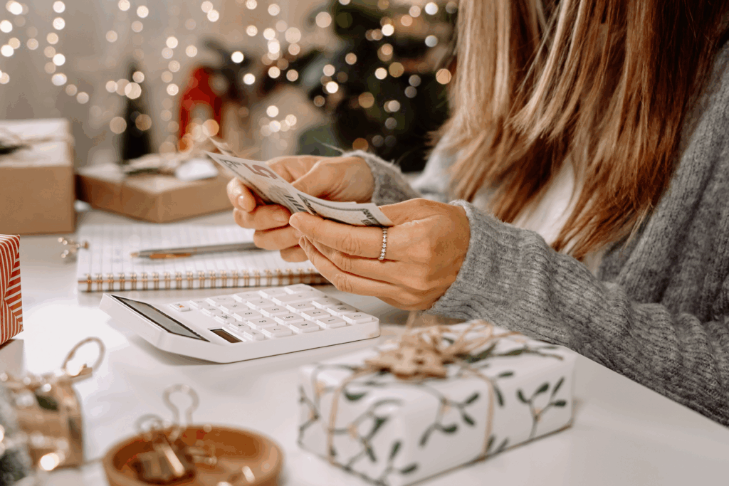 Woman counting cash while planning a holiday budget with gifts and decorations on the table.