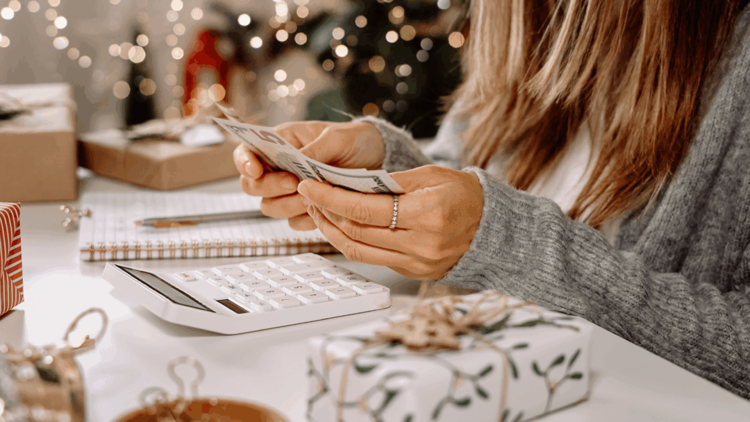 Woman counting cash while planning a holiday budget with gifts and decorations on the table.