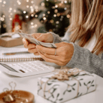 Woman counting cash while planning a holiday budget with gifts and decorations on the table.