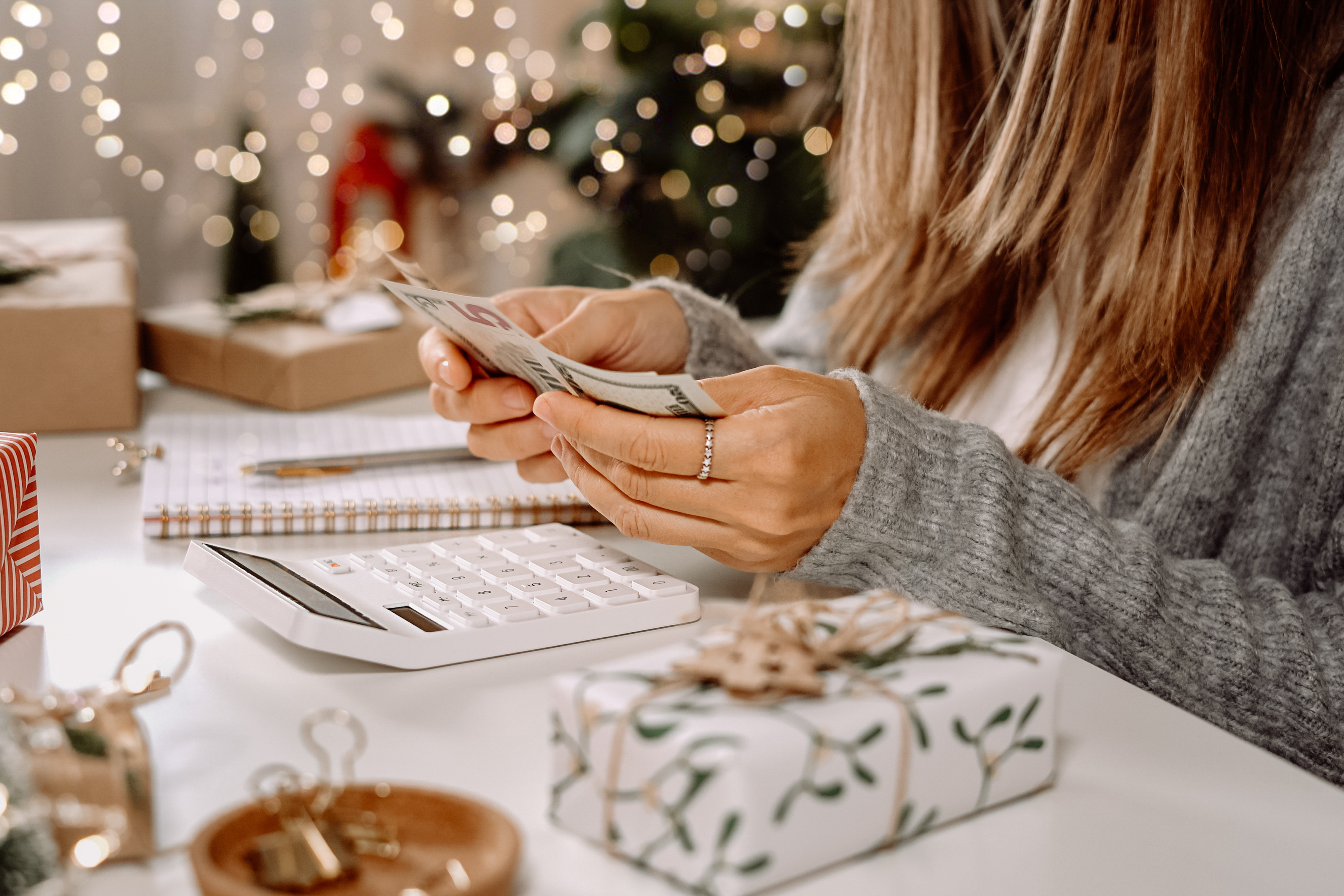 Woman counting cash while planning a holiday budget with gifts and decorations on the table.
