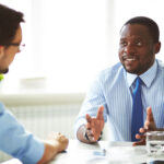 Business professional in a striped shirt speaking with a colleague during a meeting.