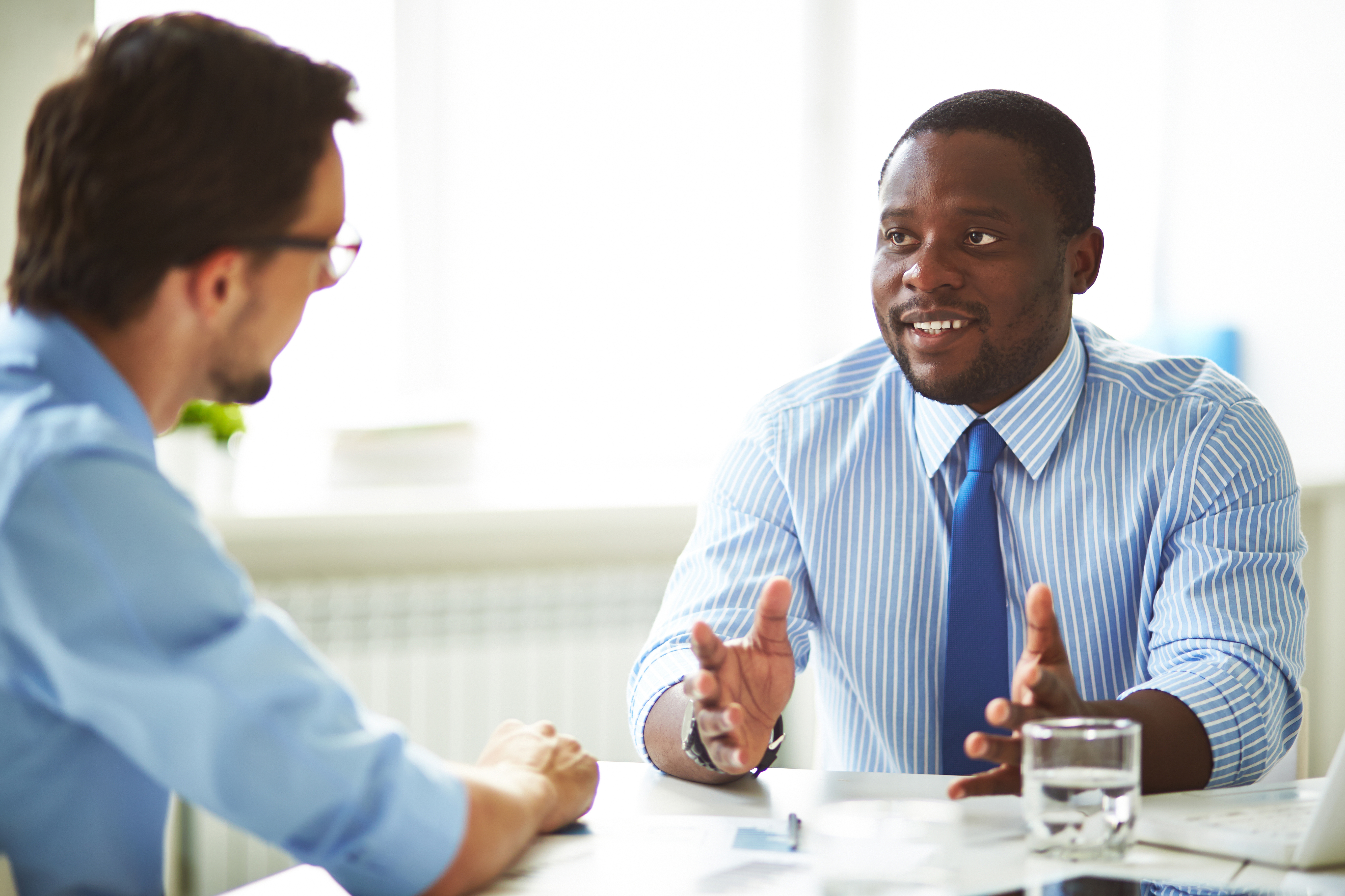 Business professional in a striped shirt speaking with a colleague during a meeting.