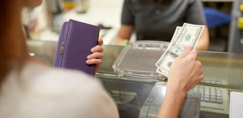 A person hands cash to a cashier across a counter while holding a purple wallet.