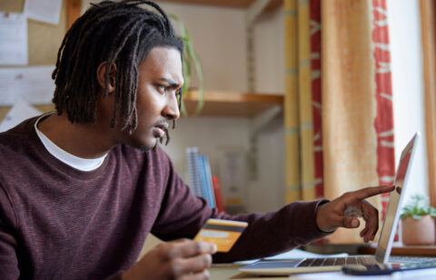 Man holding a credit card while using a laptop, focused on managing finances online.