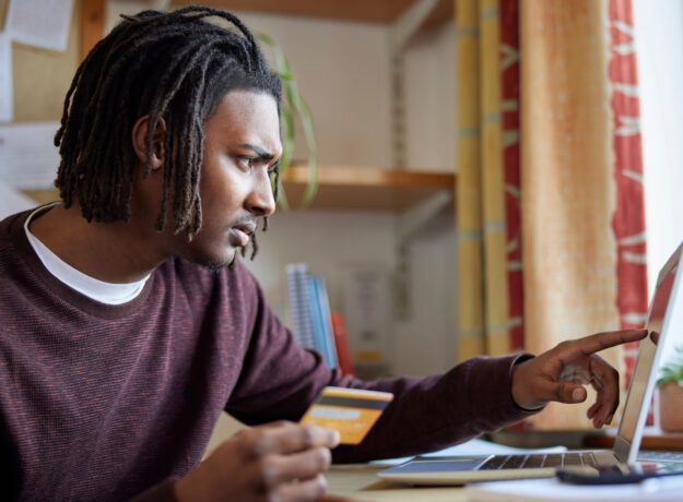 Man holding a credit card while using a laptop, focused on managing finances online.