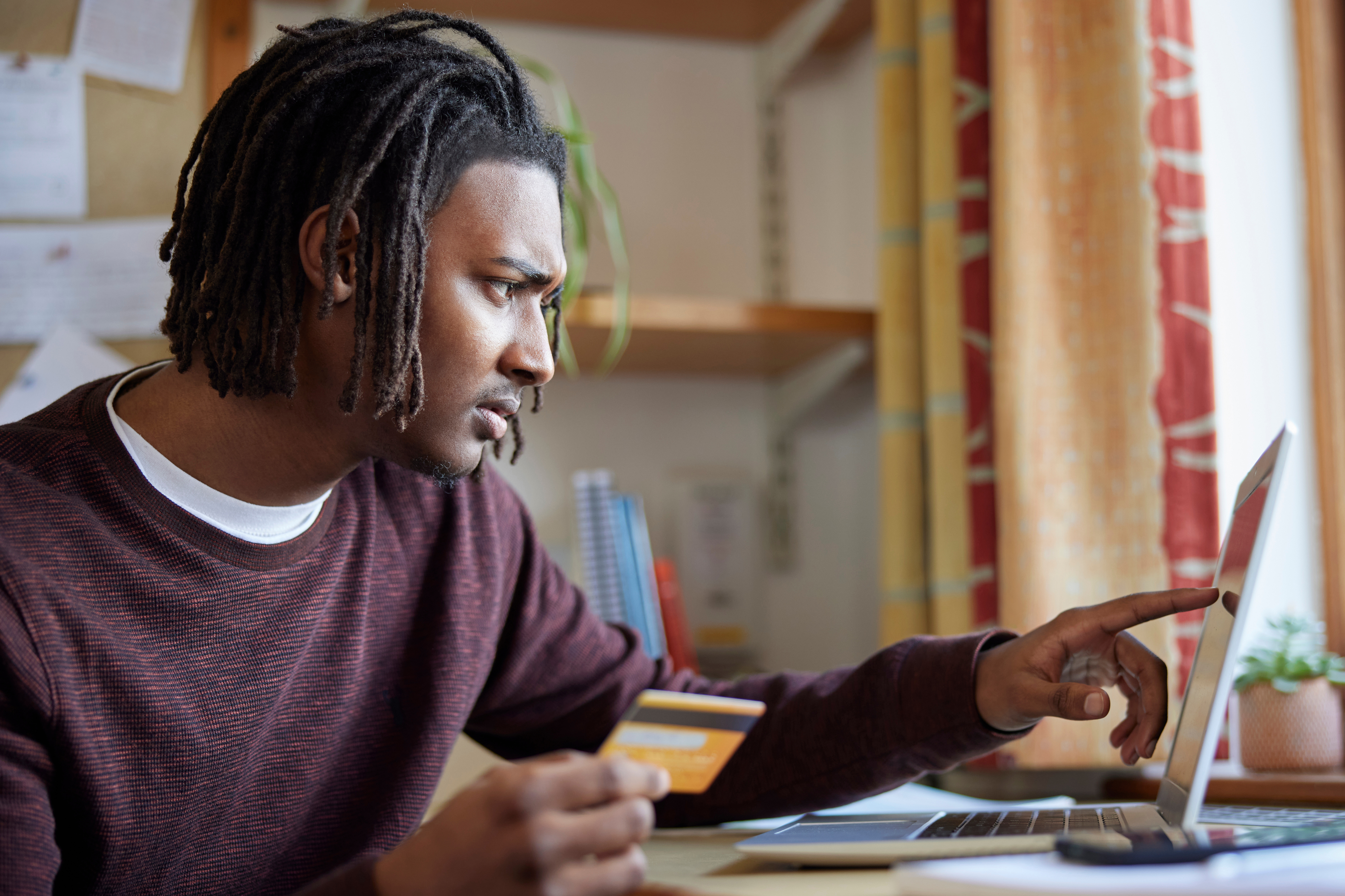 Man holding a credit card while using a laptop, focused on managing finances online.