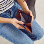 A seated person holding open an empty wallet
