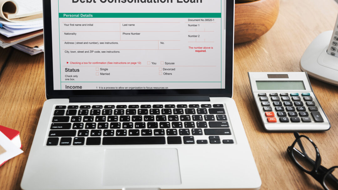 Laptop screen showing a debt consolidation loan form beside a calculator and paperwork.