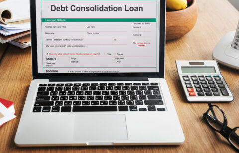 Laptop screen showing a debt consolidation loan form beside a calculator and paperwork.