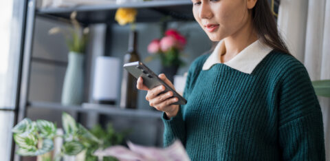 Young woman using her phone to review bills or financial documents at home.
