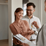 A smiling couple receives house keys from a real estate agent after buying their first home.