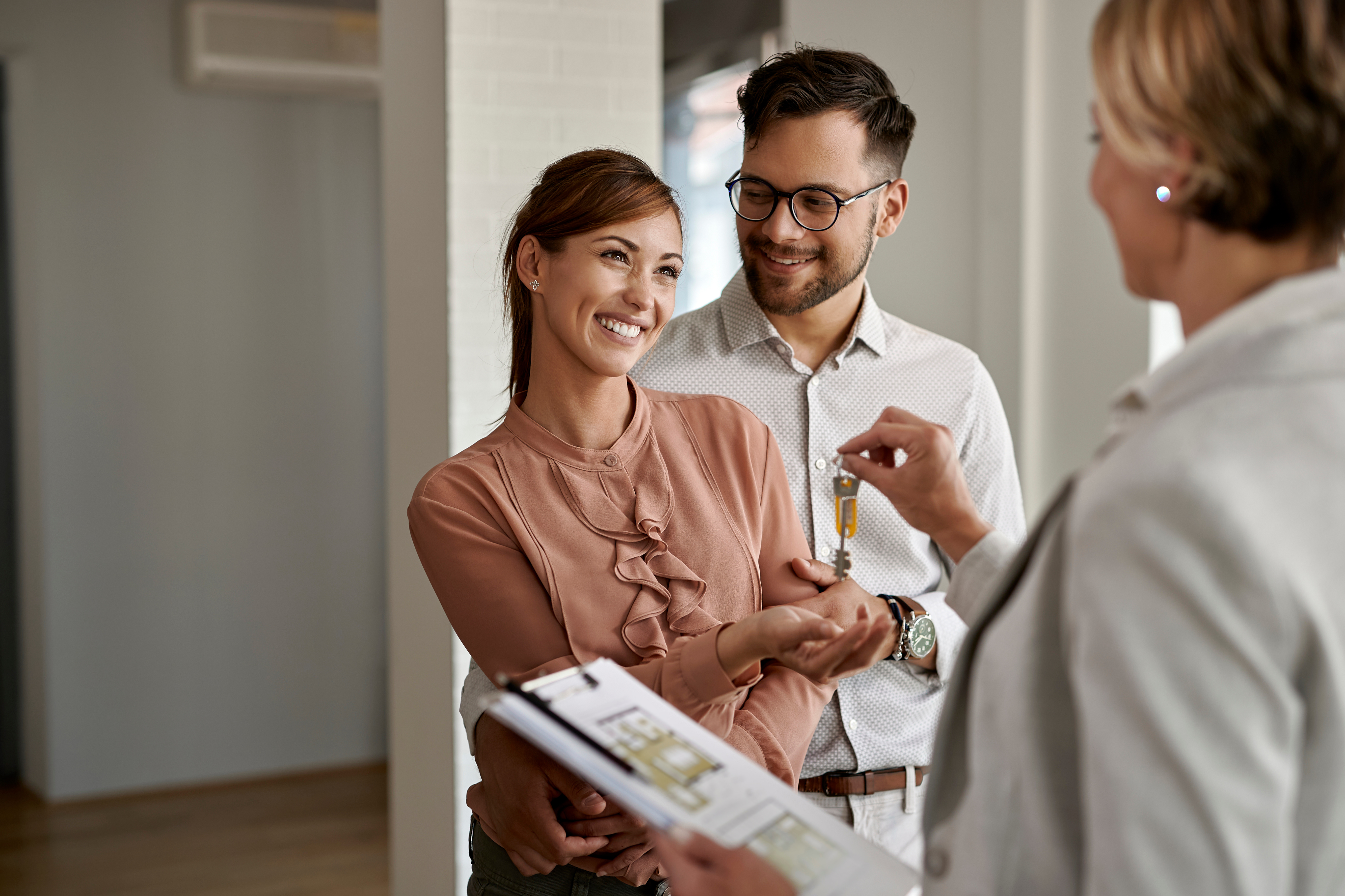 A smiling couple receives house keys from a real estate agent after buying their first home.