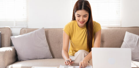 Woman using a calculator and laptop to review monthly budget at home.