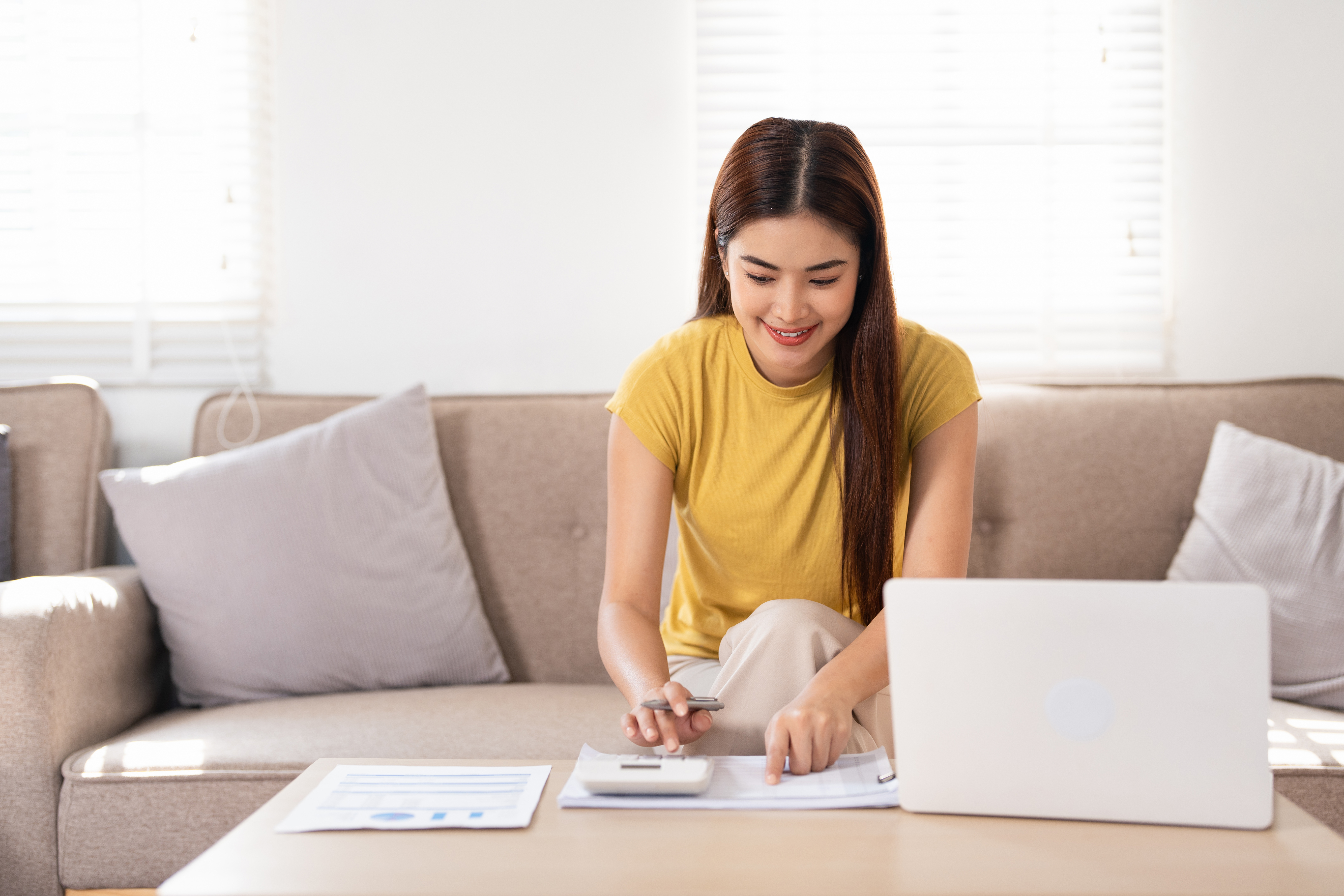 Woman using a calculator and laptop to review monthly budget at home.