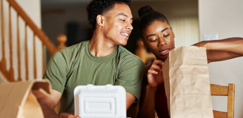 A couple sits at a dining table enjoying takeout food together at home.