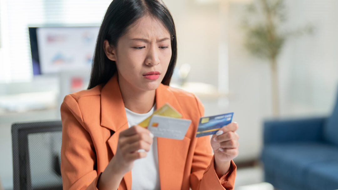 Woman looking concerned while comparing multiple credit cards at her desk.
