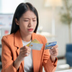 Woman looking concerned while comparing multiple credit cards at her desk.