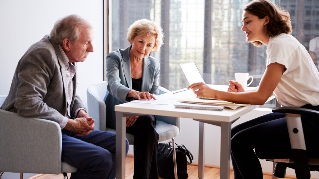 An older couple sits across from a professional in an office, reviewing financial documents together.