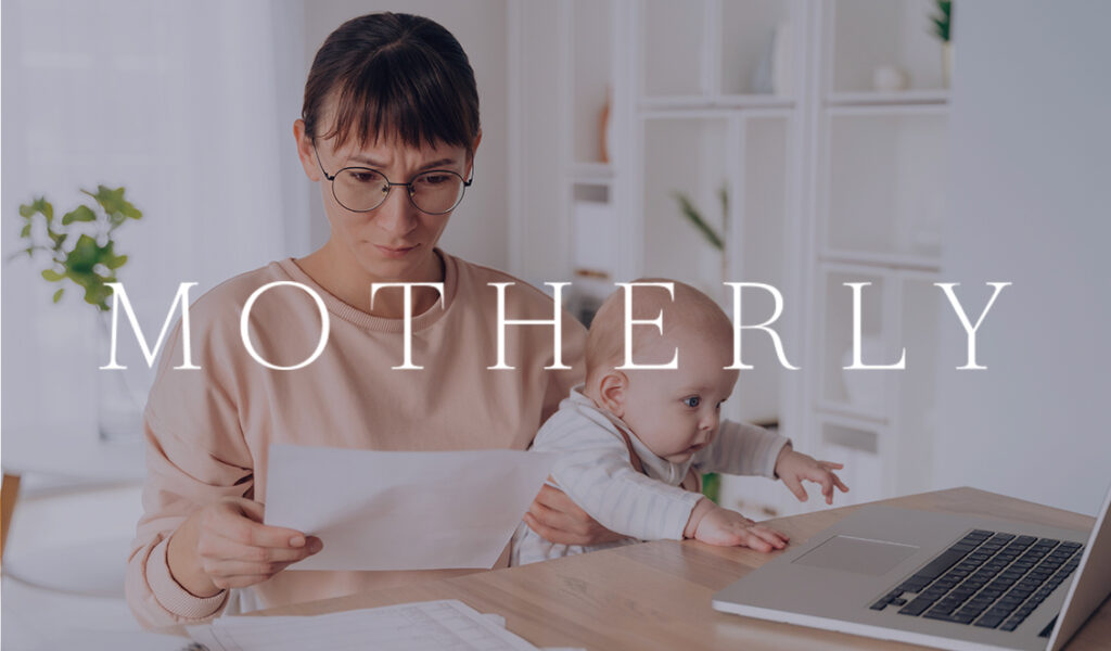 A mother holding her baby while reviewing papers at a desk with a laptop, with the Motherly logo overlayed on the image.