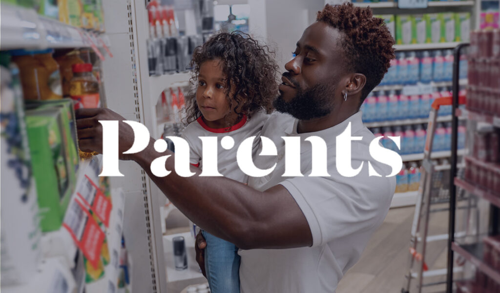A father holds his young child while shopping in a grocery store aisle, with the Parents logo displayed across the image.