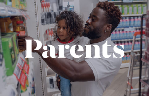 A father holds his young child while shopping in a grocery store aisle, with the Parents logo displayed across the image.