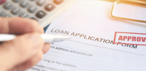 Close-up of a loan application form with an approved stamp and a hand holding a pen.