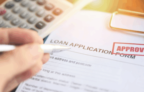 Close-up of a loan application form with an approved stamp and a hand holding a pen.