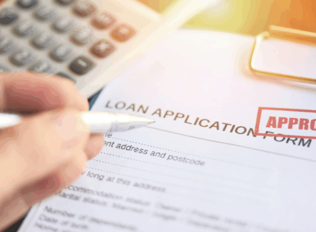 Close-up of a loan application form with an approved stamp and a hand holding a pen.