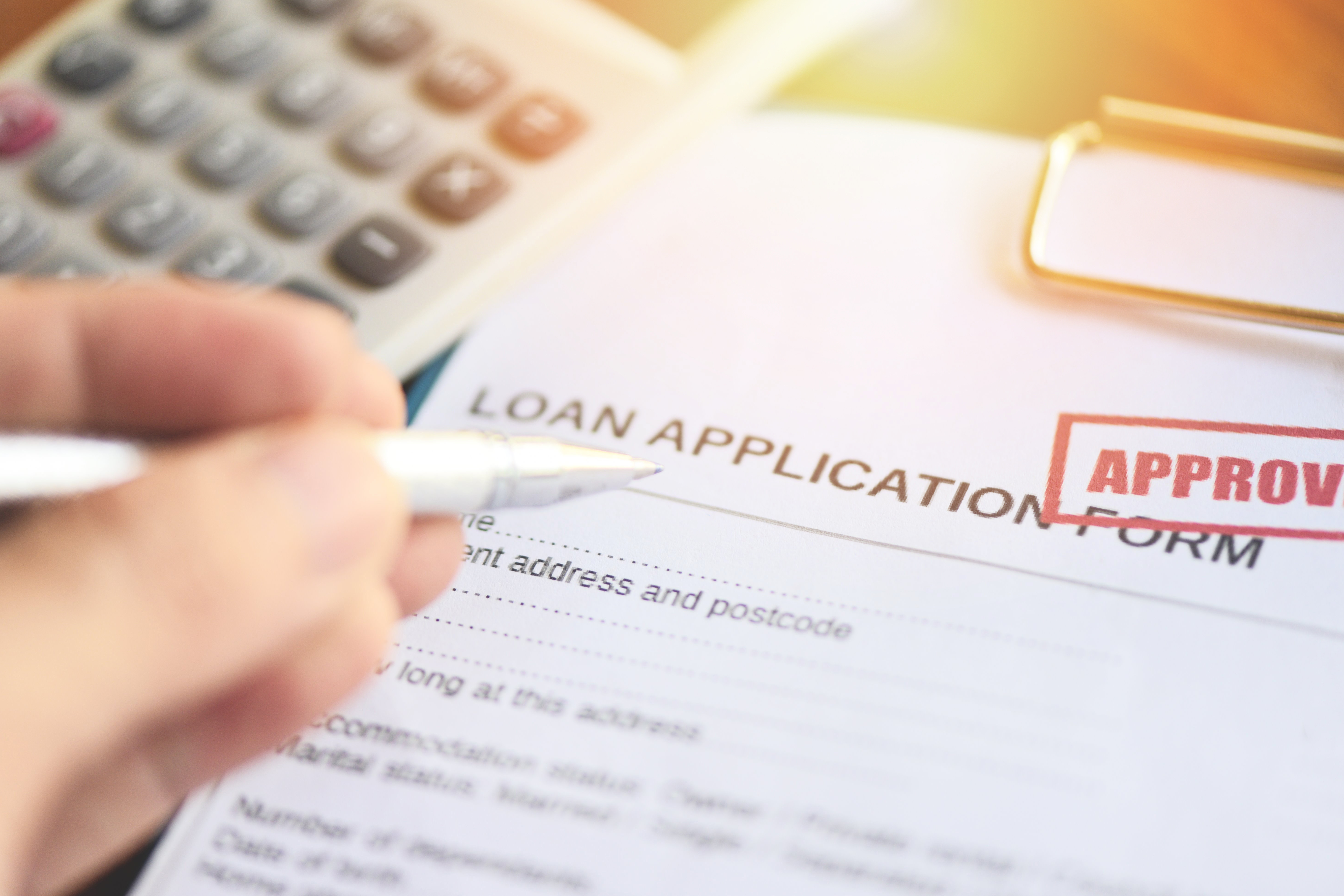 Close-up of a loan application form with an approved stamp and a hand holding a pen.