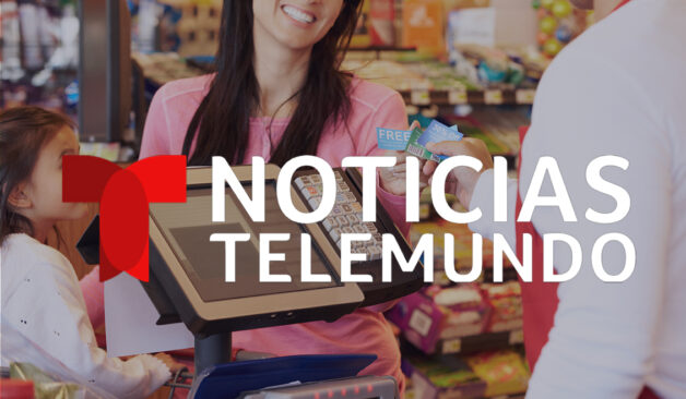 A smiling woman pays at a grocery store checkout while holding coupons, with a child beside her. The Noticias Telemundo logo is displayed over the image.