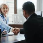 Smiling businesswoman in a meeting shaking hands with a client across a desk.