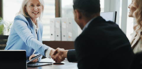 Smiling businesswoman in a meeting shaking hands with a client across a desk.