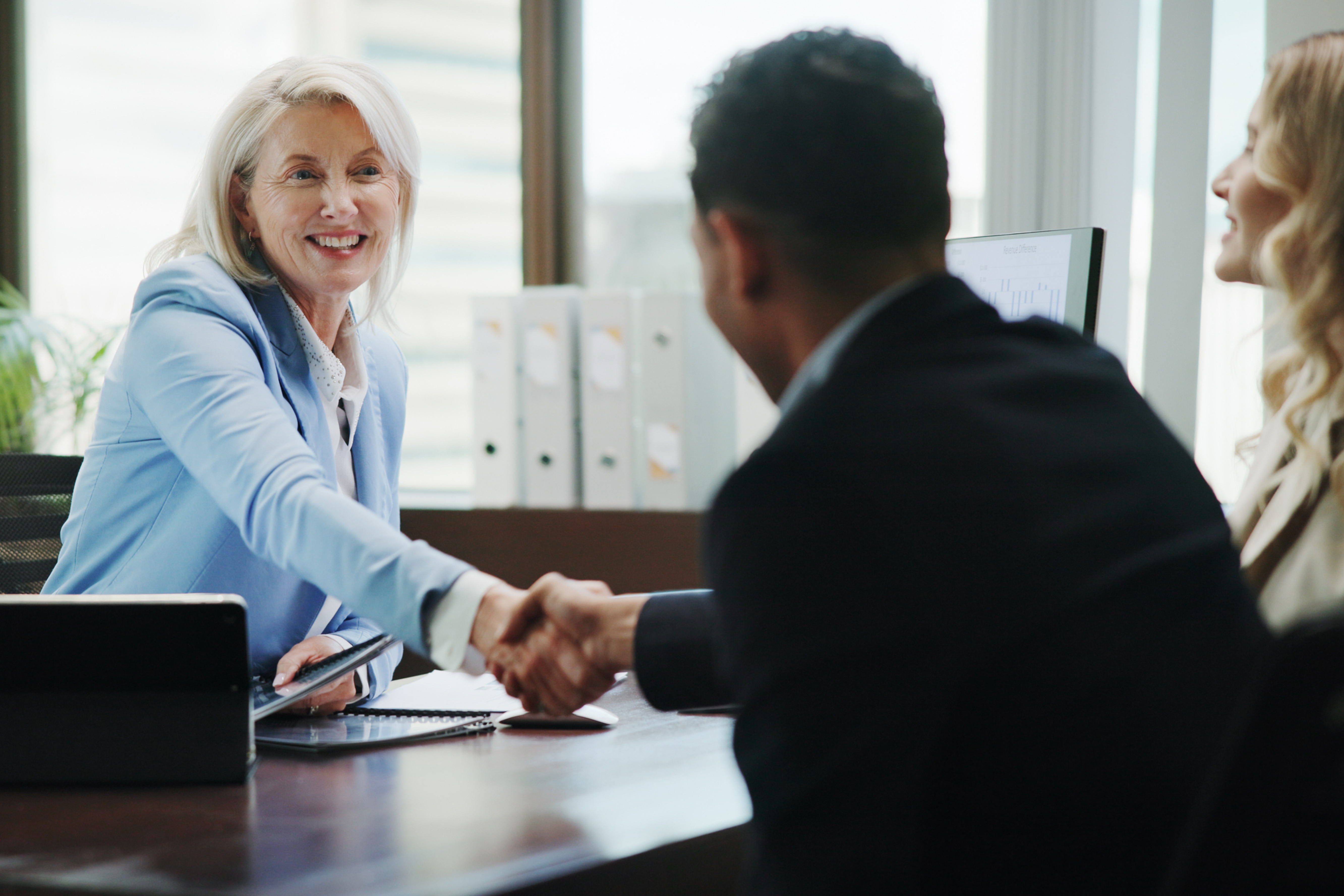 Smiling businesswoman in a meeting shaking hands with a client across a desk.