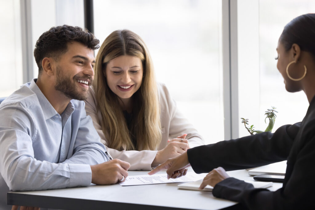 Smiling couple meeting with a professional to review and sign financial documents.