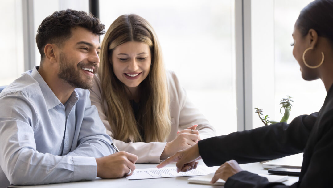Smiling couple meeting with a professional to review and sign financial documents.