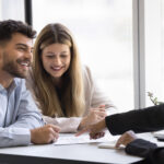 Smiling couple meeting with a professional to review and sign financial documents.