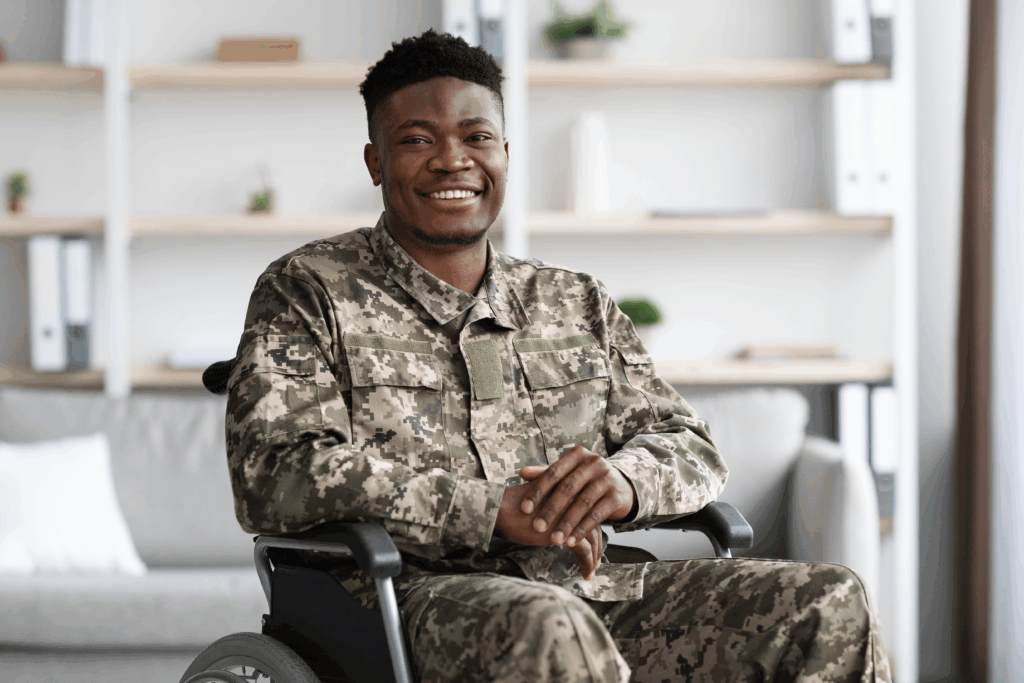 Veteran in camouflage uniform seated in a wheelchair, smiling at the camera.