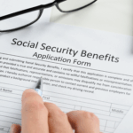 A person reviews a Social Security Benefits application form with a pen and paperwork nearby.