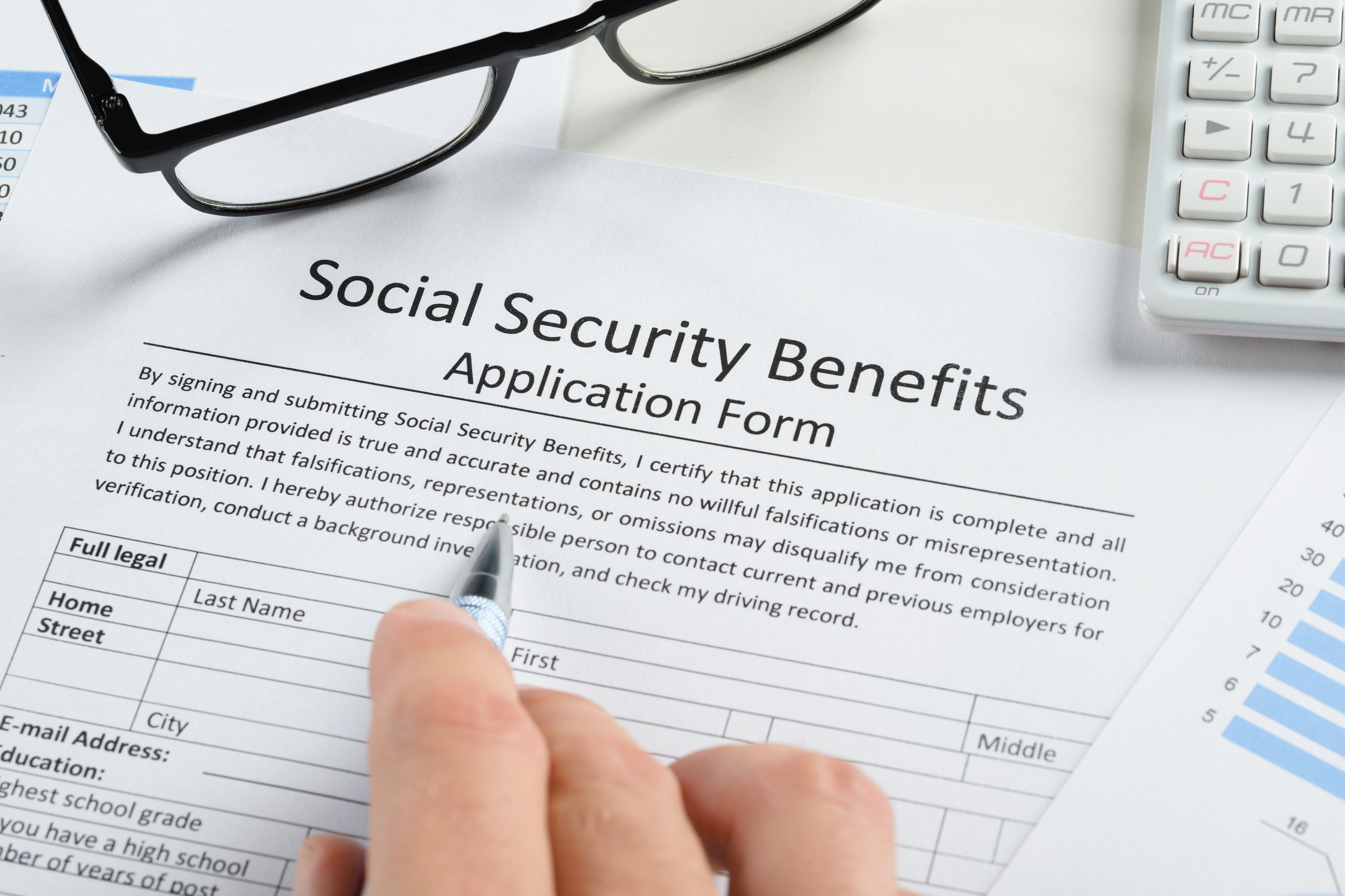 A person reviews a Social Security Benefits application form with a pen and paperwork nearby.